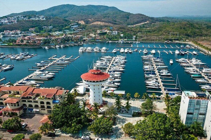 A marina with numerous boats docked, a lighthouse, and surrounding buildings. 2