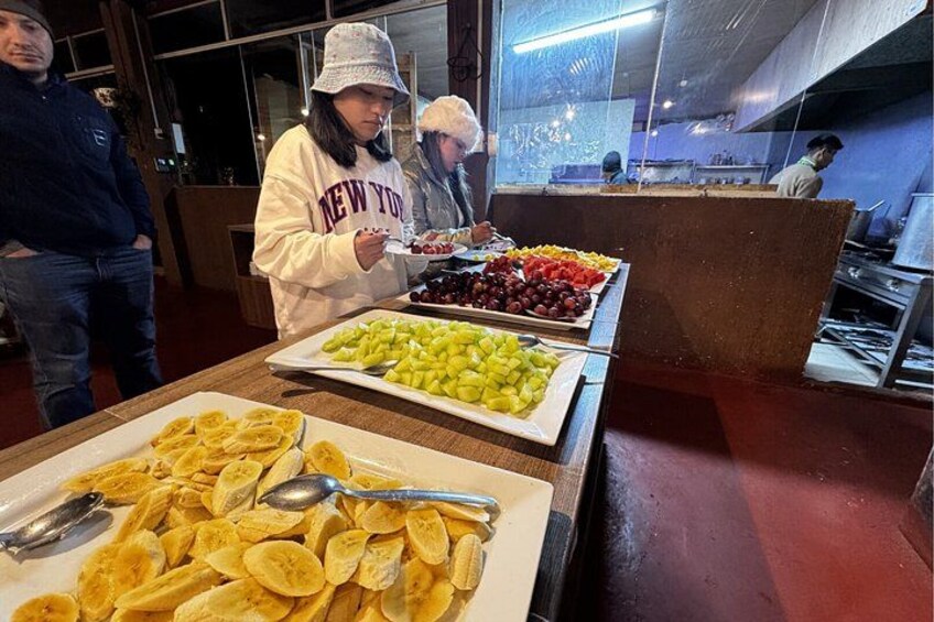A buffet with various food items including fruits, chips, and a person serving. 2