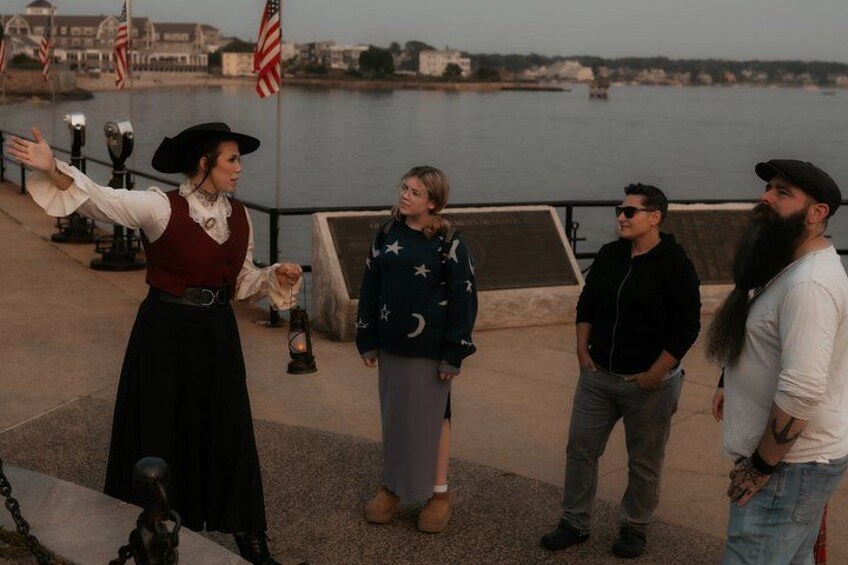 A person in historical attire gesturing, a person in a star-patterned sweater, and two casually dressed individuals by a waterfront. 4