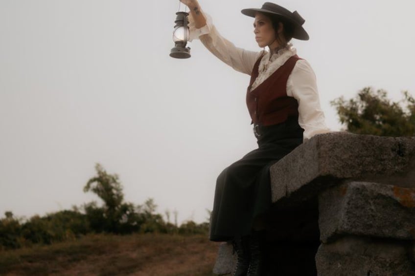 A person in historical attire sitting on a stone wall, holding a lantern. 5