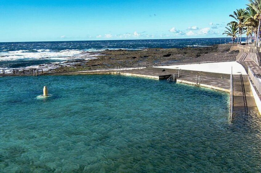 A clear blue pool with a jet ski, a rocky shoreline, and a palm tree-lined walkway. 3