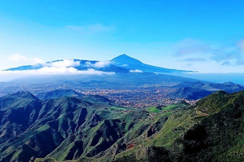 A mountain with a cloud cover, a valley with a town, and green hills. 2