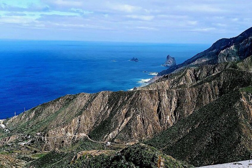 A coastal landscape with steep cliffs, a clear blue sea, and a rocky outcrop in the distance. 4