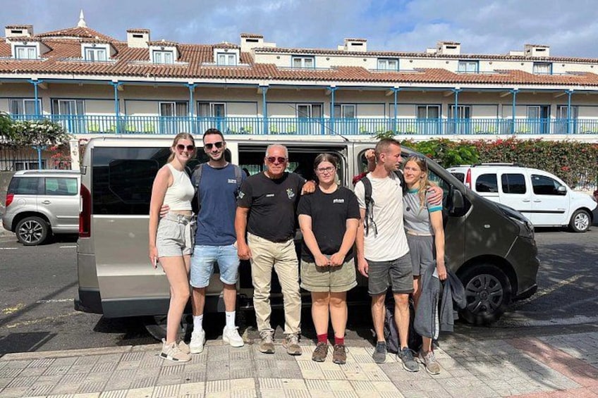A group of people standing in front of a van with a building in the background. 3