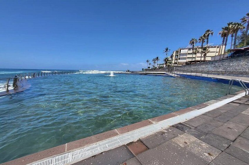 A coastal swimming area with clear water, a diving board, and a stone walkway. 2