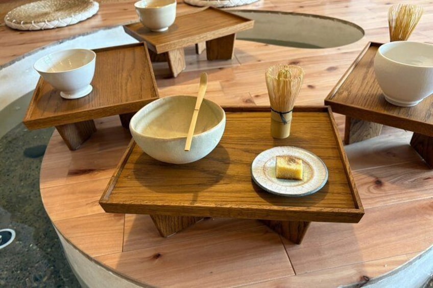 A traditional Japanese tea ceremony setup with wooden tables, bowls, and a whisk. 1