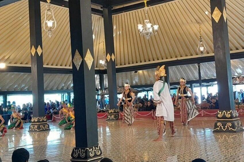 A cultural performance with dancers in traditional costumes under a large, tent-like structure with patterned columns. 5