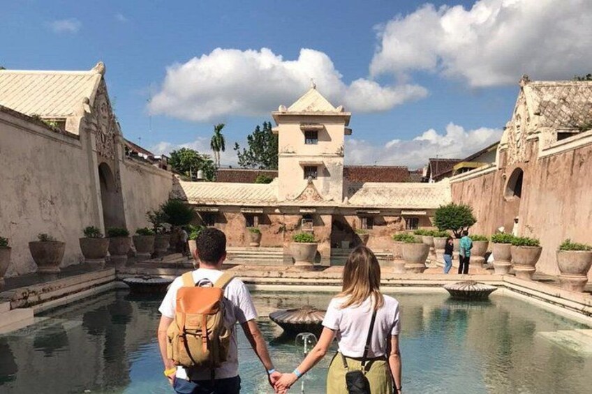 A couple holding hands in a courtyard with a pool, surrounded by historic buildings. 4