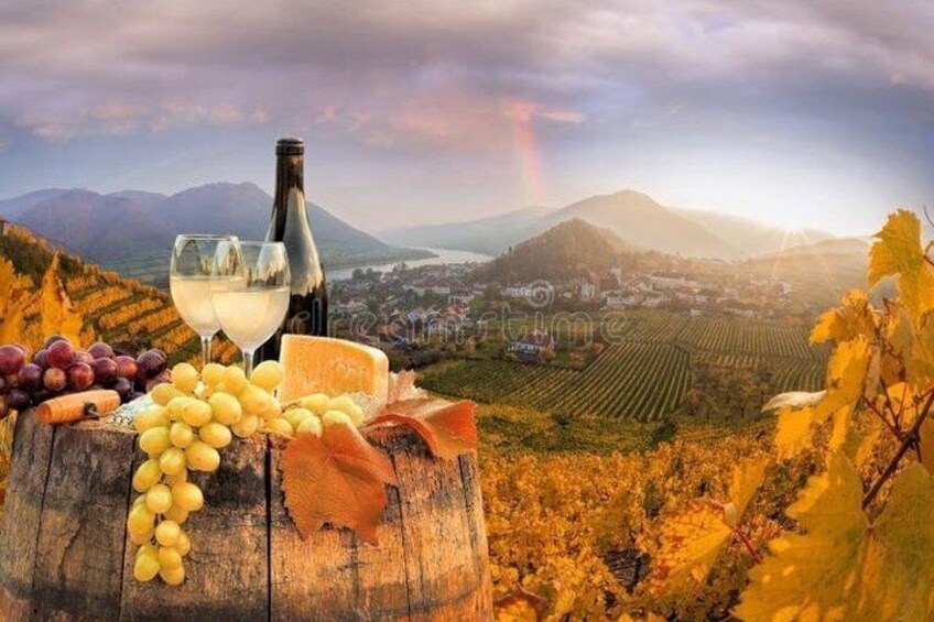 A wooden barrel with grapes, cheese, a bottle of wine, and glasses on a hillside with vineyards and mountains in the background. 5