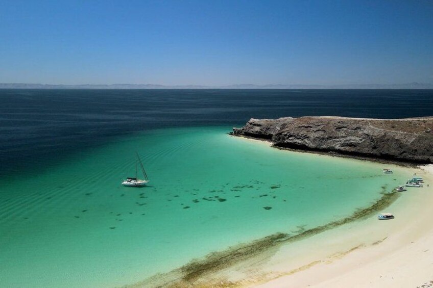 A coastal landscape with clear turquoise waters, a sandy beach, and a rocky outcrop. 2
