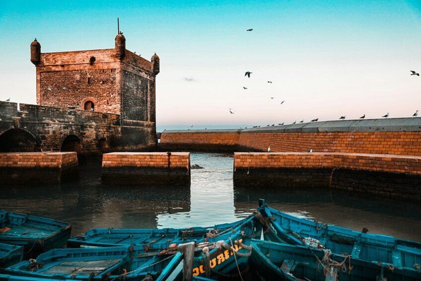 A historic stone tower, a calm waterway, and several boats docked near the shore. 5