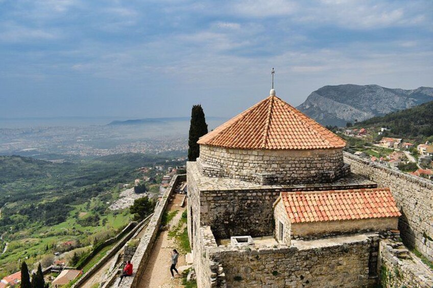 A stone tower with a red roof, overlooking a valley and distant cityscape. 1