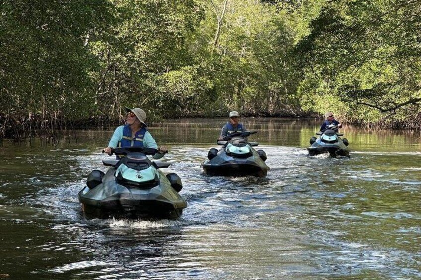 Tre personer på jetski i et mangroveområde. 1