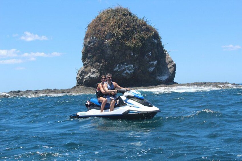 Un jet ski avec deux personnes à bord, de l’eau et une grande formation rocheuse en arrière-plan. 4