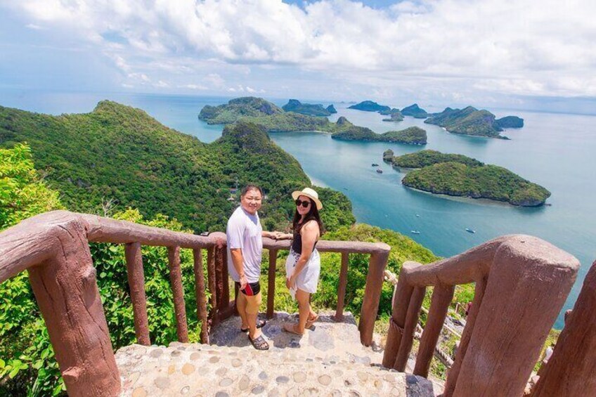 A couple standing on a stone staircase with a view of a coastal landscape with islands. 1
