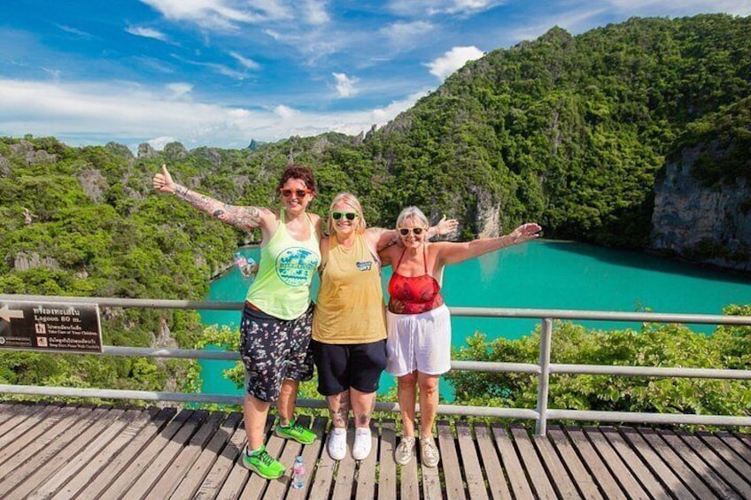 Three people standing on a wooden deck with a scenic view of a turquoise lake and green forest. 5