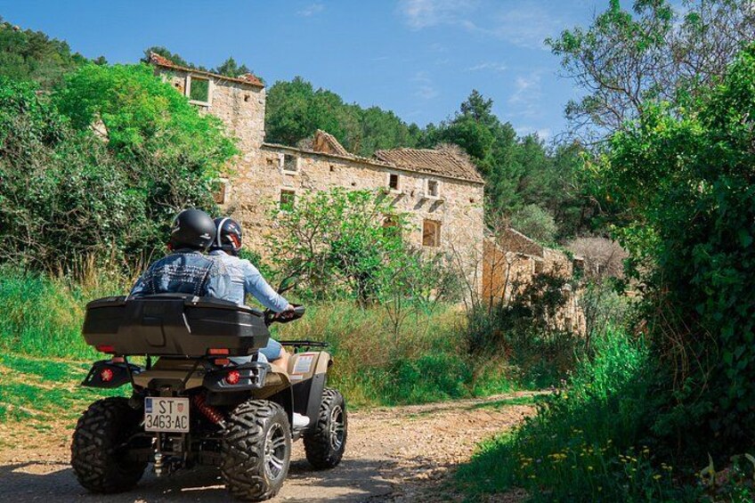 A person riding an ATV on a dirt path with stone buildings in the background. 2