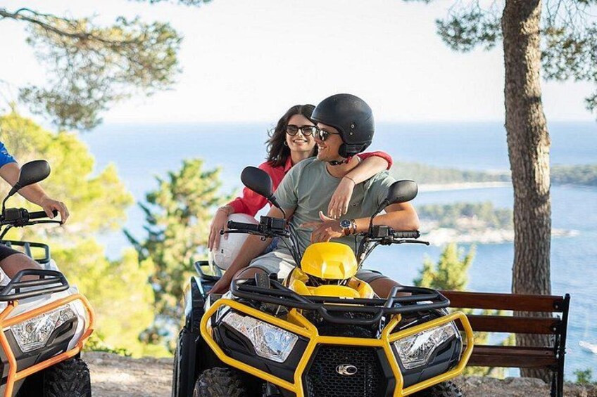 Two people on a yellow ATV with a scenic coastal background. 1