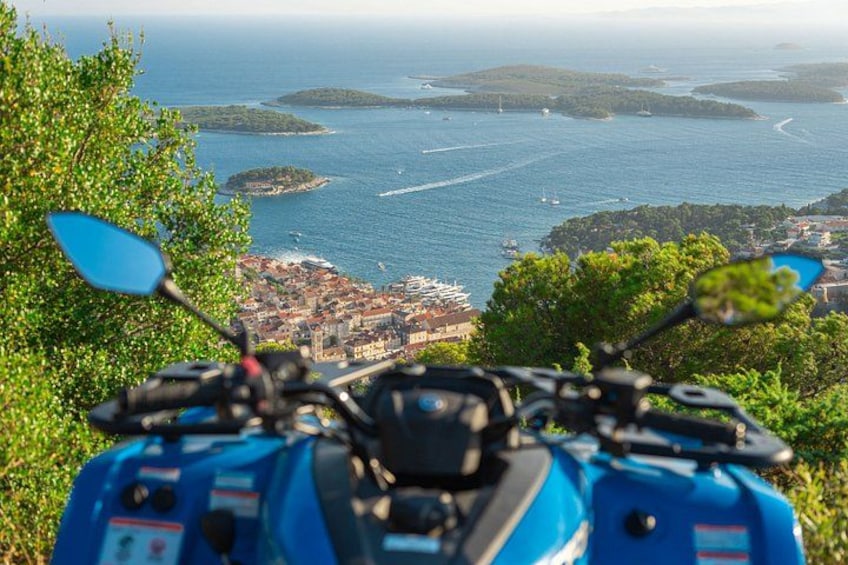 A blue scooter with a view of a coastal town and islands in the distance. 4