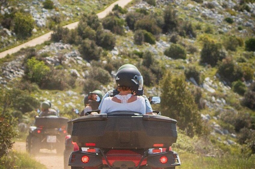 A group of people on off-road vehicles on a dirt path surrounded by rocky terrain and sparse vegetation. 3