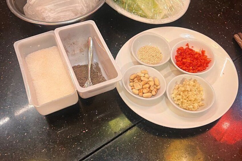 A table with various food ingredients including white sugar, brown sugar, sesame seeds, red bell peppers, and garlic. 3