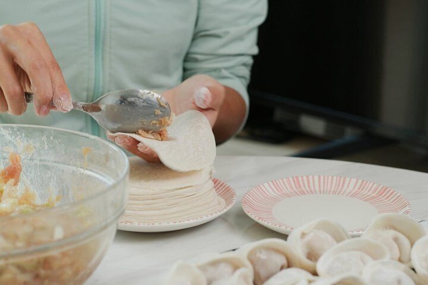 A person preparing food, specifically filling dumplings with a mixture in a bowl. 2