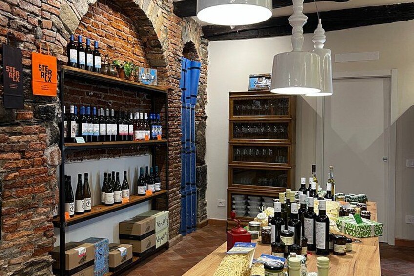 A wine shop with shelves of bottles, a wooden table with more bottles, and hanging lights. 2