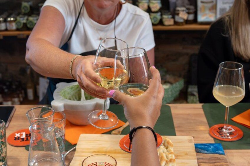 Una persona sosteniendo una copa de vino, otra persona con una copa de vino blanco, y una mesa con varios objetos, incluyendo una tabla de cortar y una botella. 4