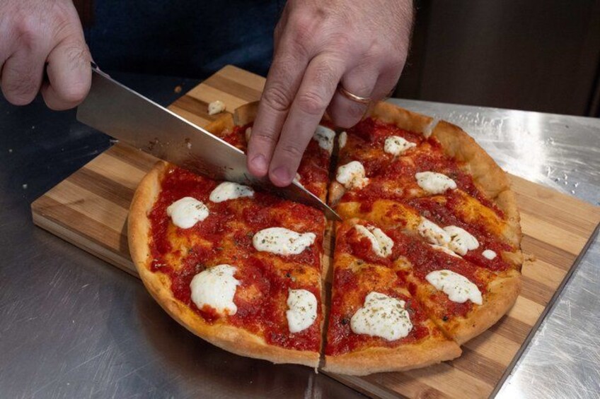 Una persona cortando una pizza sobre una tabla de madera. 2