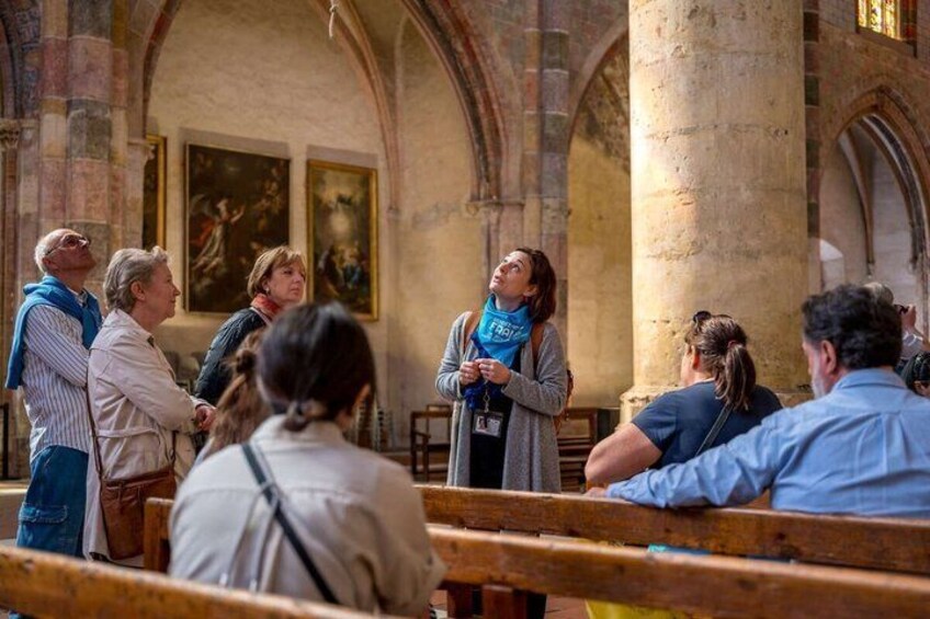 A group of people inside a church with stone columns and paintings on the walls. 4