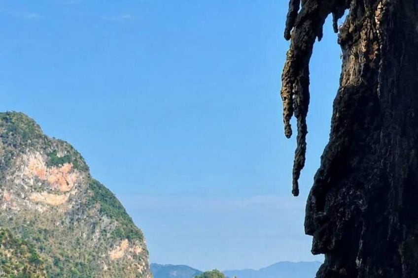 A rocky cliff with a cave opening, a distant mountain range, and a clear blue sky. 5