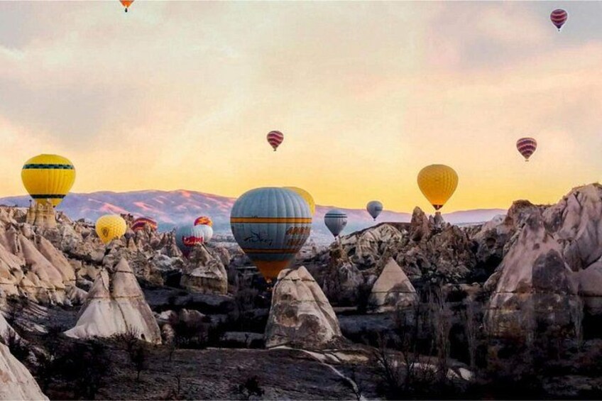 A landscape with numerous hot air balloons, rocky terrain, and a mountainous backdrop. 5