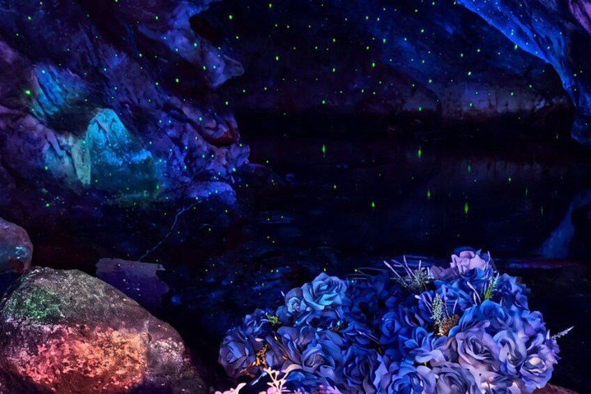 A cave with glowing blue and green lights, a large rock, and a floral arrangement. 3