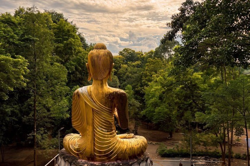 A large golden Buddha statue seated in a meditative pose surrounded by lush greenery. 1