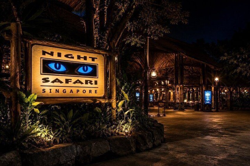 A sign for a night safari in Singapore, surrounded by trees and a wooden structure. 3