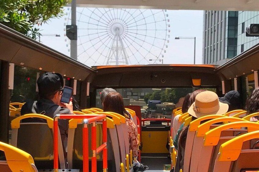 A bus interior with passengers seated, a Ferris wheel in the background, and a building with a glass facade. 4