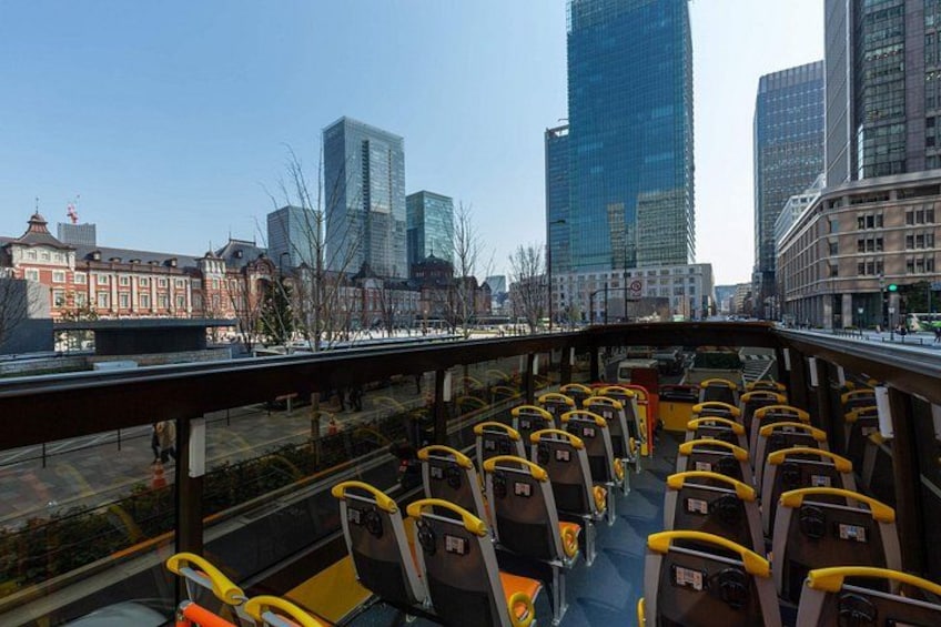 A bus with yellow seats and a metal railing, traveling on a road with buildings in the background. 3