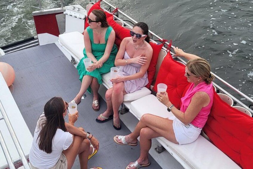 A group of people on a boat with red cushions, some holding drinks. 3