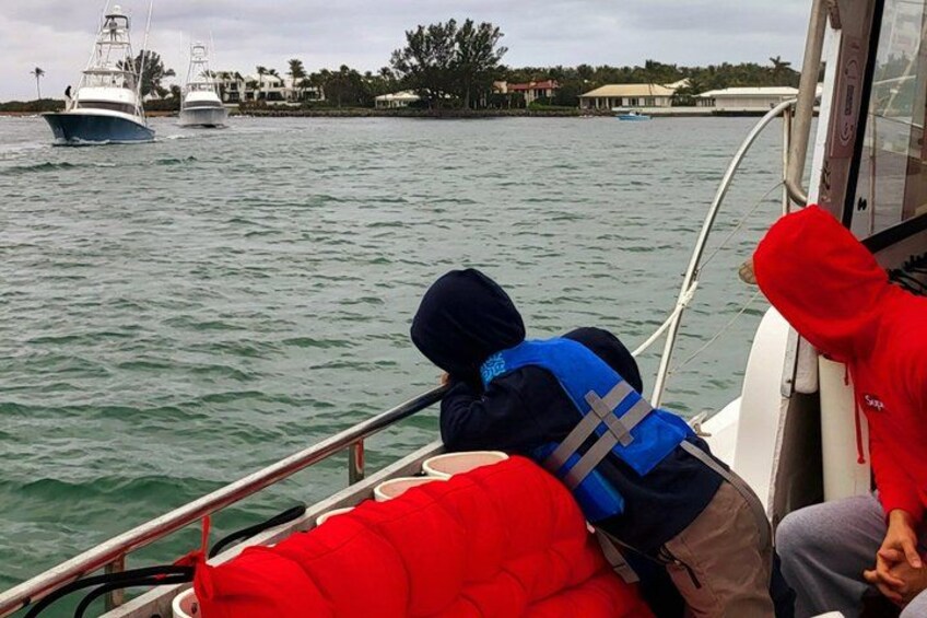 A boat with two people wearing life jackets, a calm water body, and distant buildings along the shore. 2