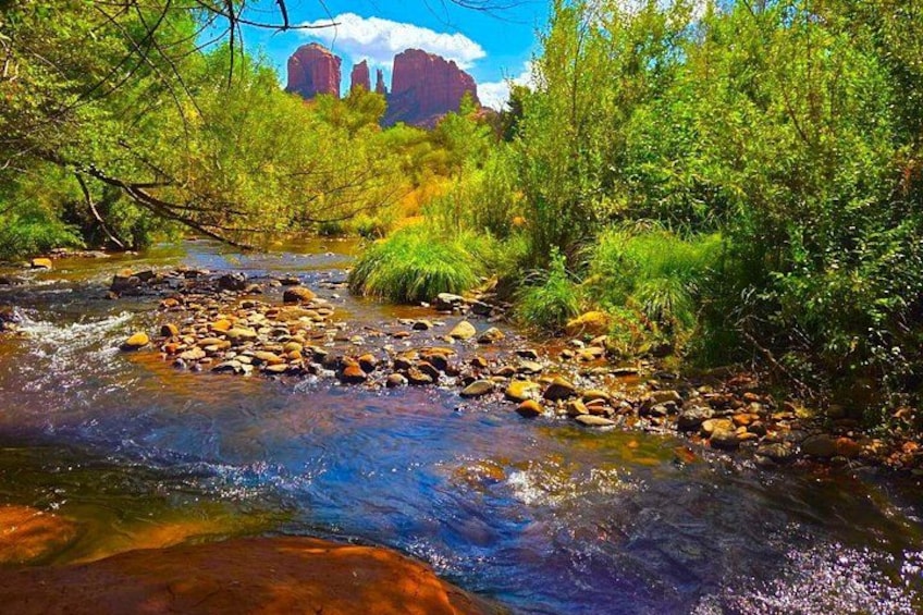 A river with rocks, greenery, and red rock formations in the background. 3