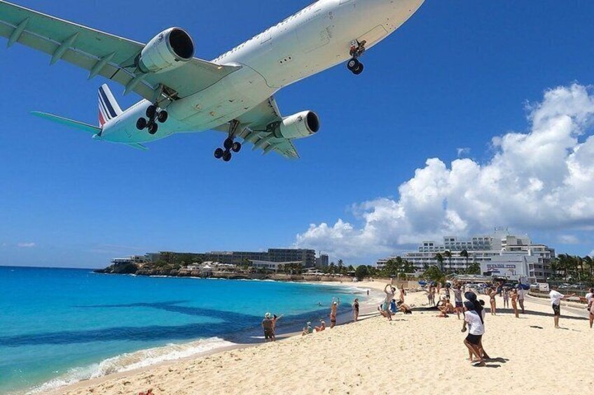 A beach with people, a plane landing, and buildings in the background. 5