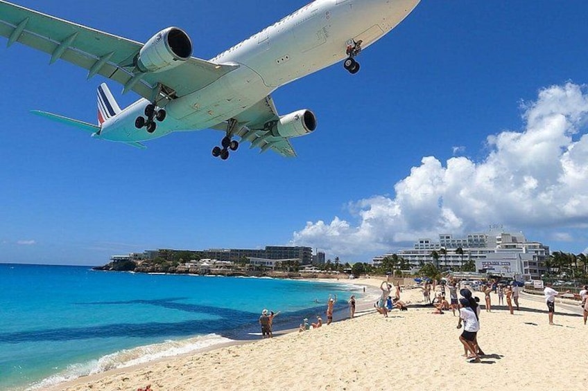 A beach with people, a plane landing, and buildings in the background. 5