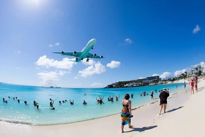 A beach with people, a plane flying overhead, and buildings in the background. 4