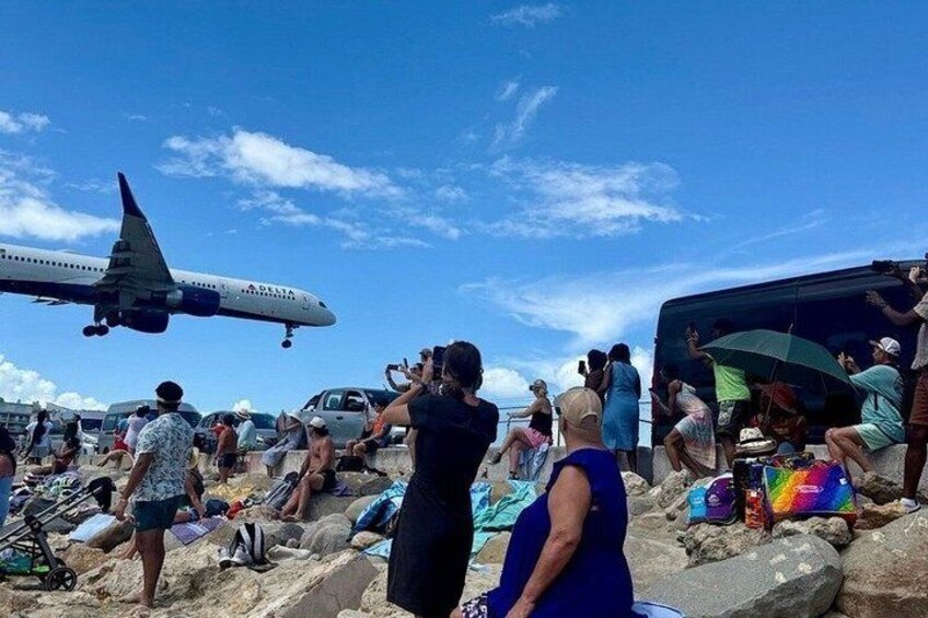 A beach with people, a parked van, and a Delta airplane in the background. 1