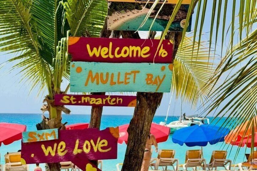 A beach with a sign reading 'Welcome to Mullet Bay' and 'We Love St. Maarten.' 3