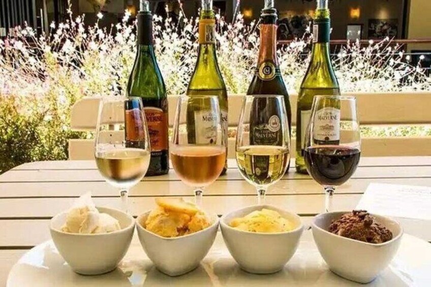 A table with four wine glasses and bowls of food, with wine bottles in the background. 1