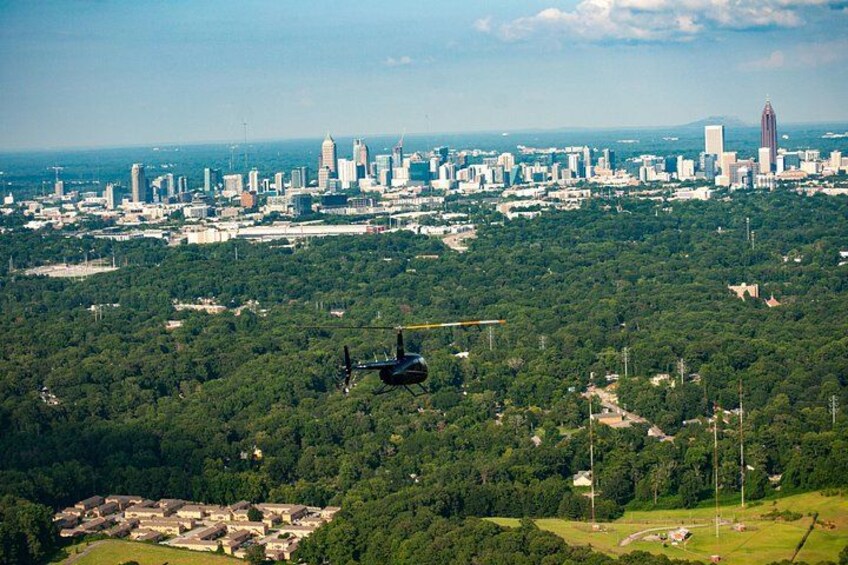 A helicopter flying over a city with a dense forest below. 1