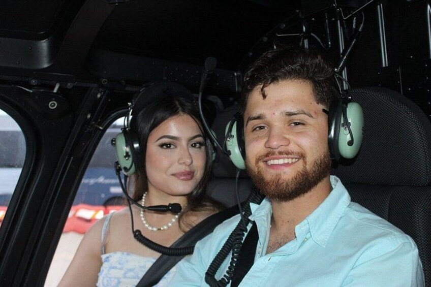 A person in a light blue shirt and another in a blue dress with a pearl necklace, both wearing headphones, seated in a vehicle. 4