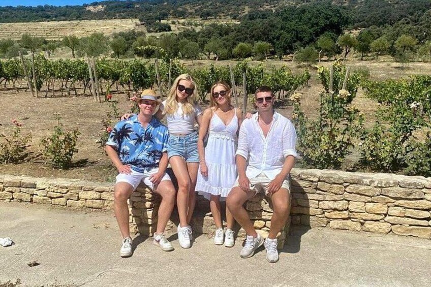 Four people sitting on a stone wall in a vineyard. 1