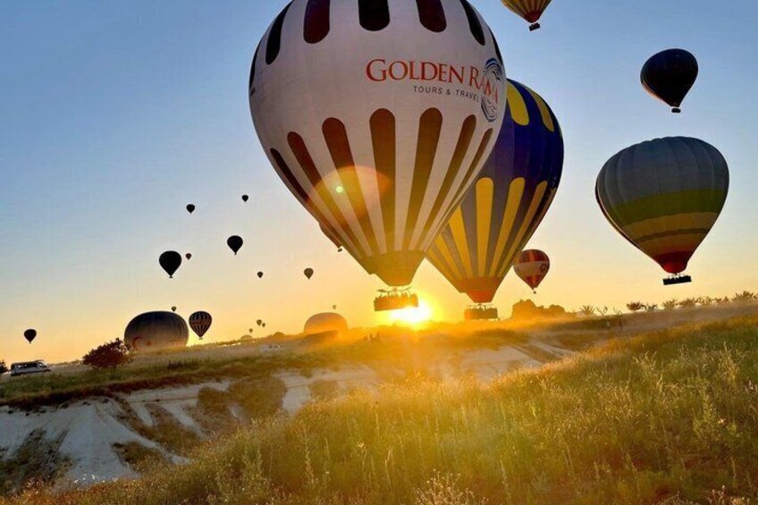 Hot air balloons over a grassy field with the sun setting in the background. 5